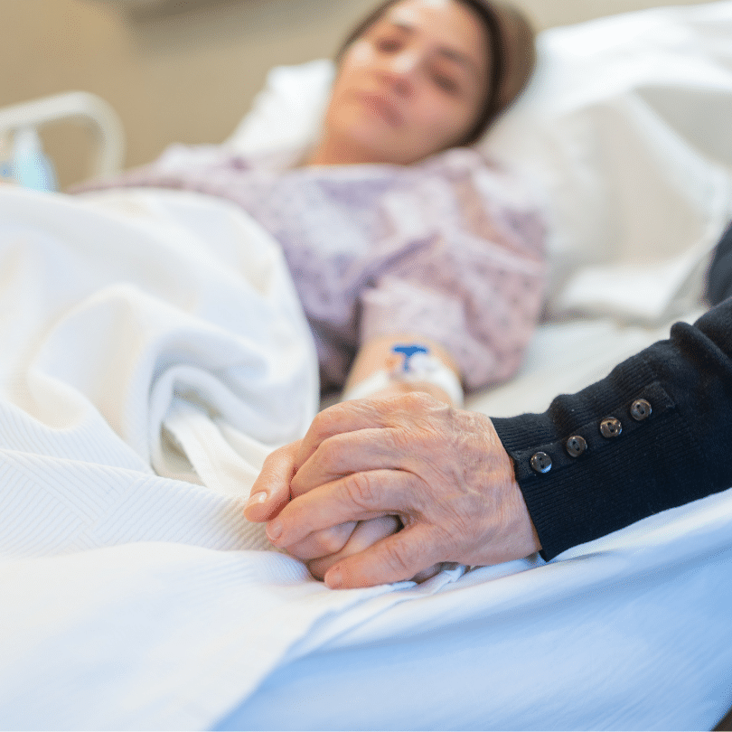 a imagem mostra uma mulher deitada em leito de hospital de mãos dadas com um acompanhante